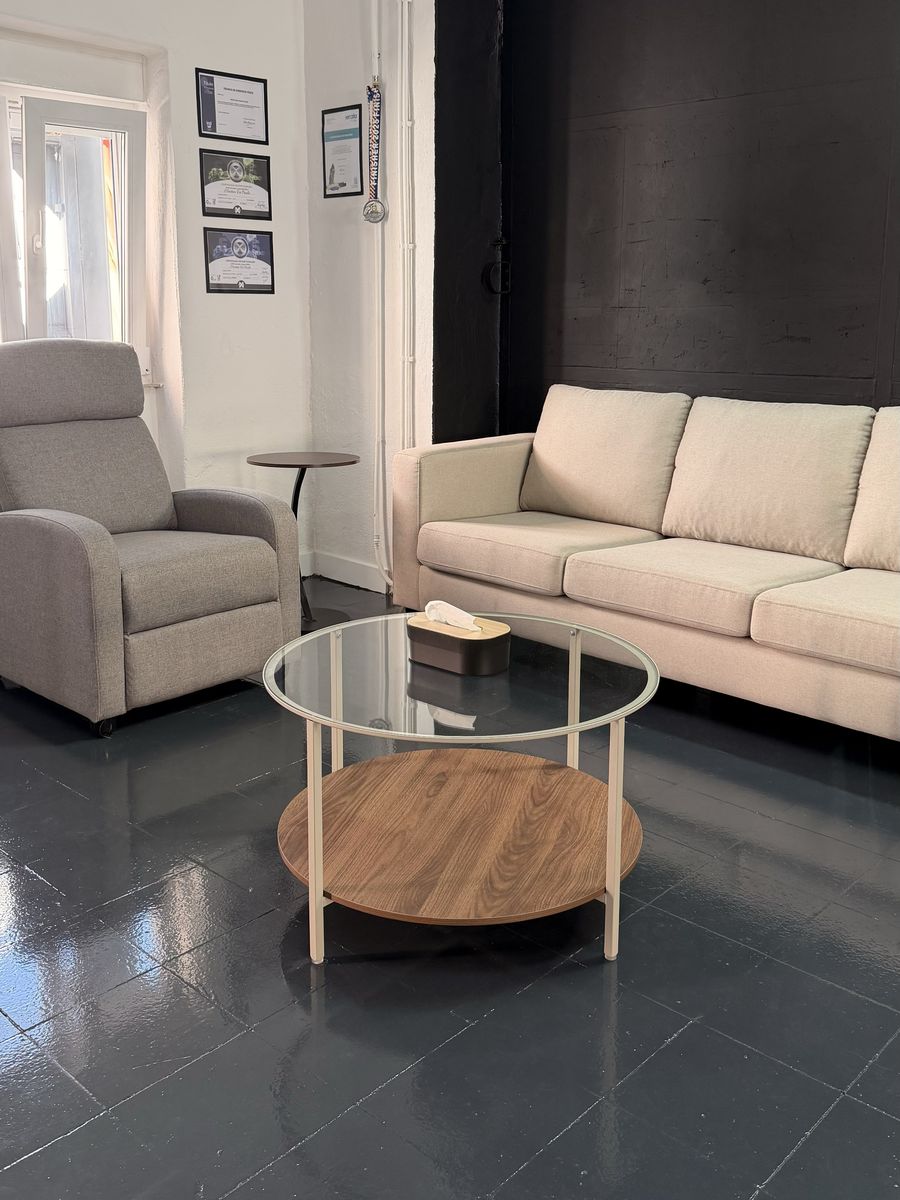 Lounge do estúdio: sofá e cadeirão em tecido claro, mesa de centro em vidro e as certificações na parede.